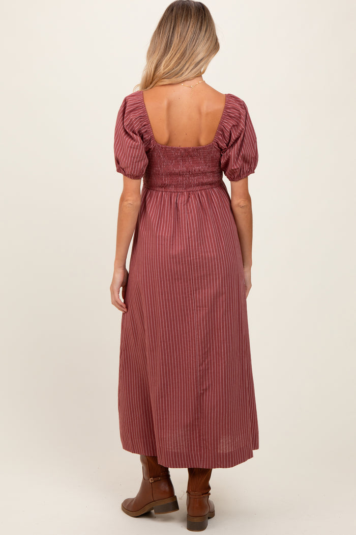 woman wearing a burgundy striped maternity dress with puff sleeves and a smocked back, standing sideways