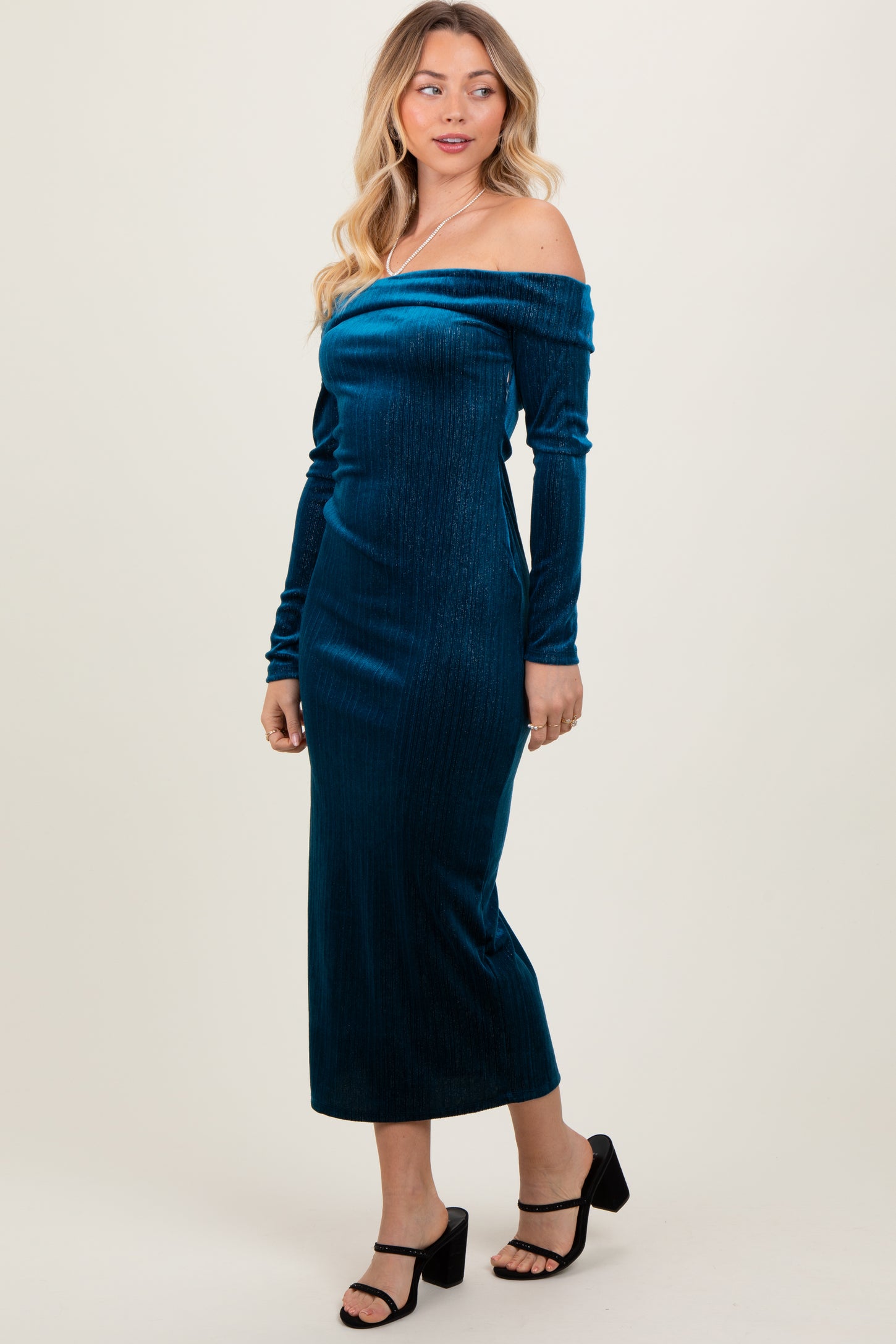 woman wearing a teal off-the-shoulder velvet midi dress with long sleeves and a fitted silhouette