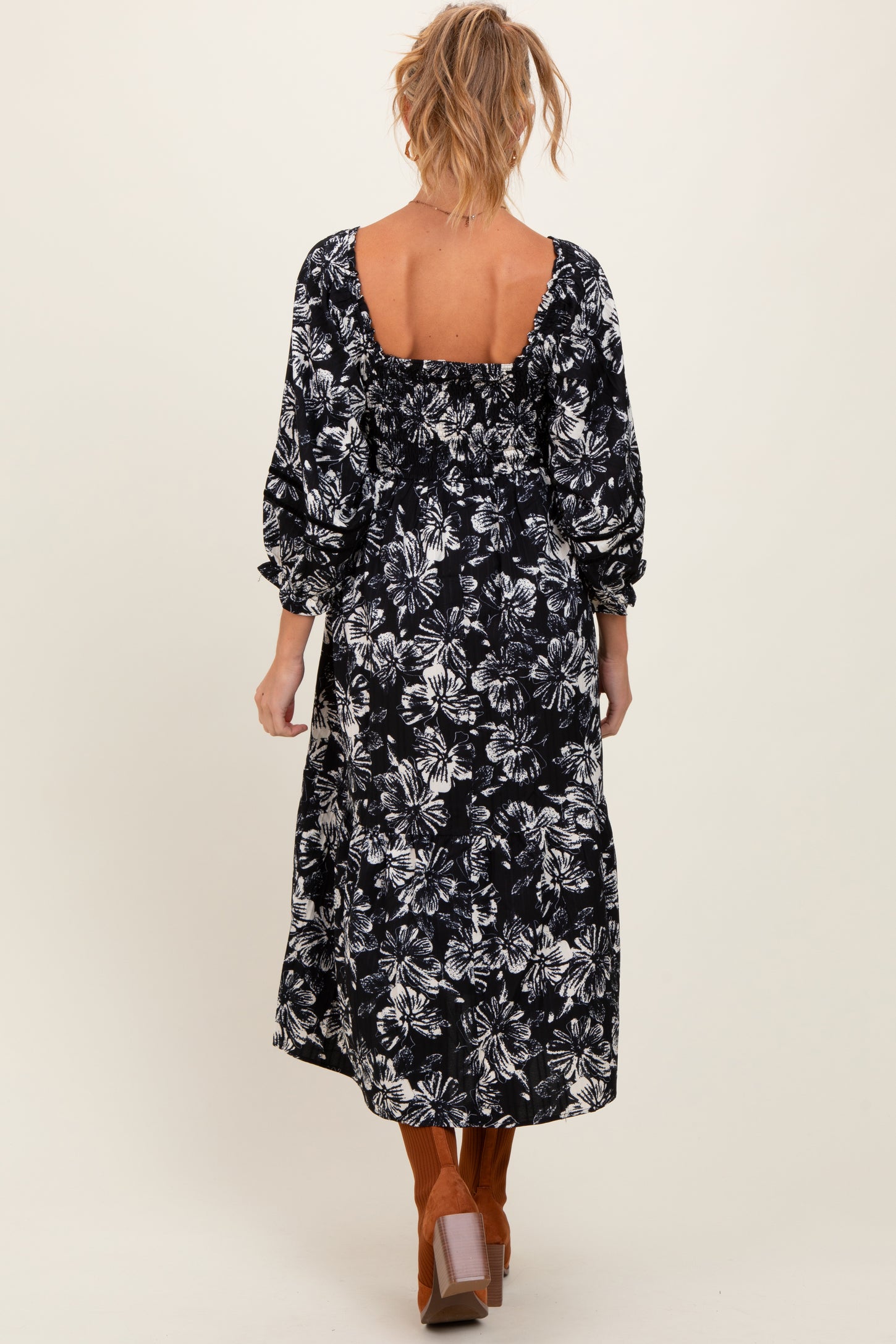 woman wearing a black floral print maternity maxi dress with puffy sleeves and an open back