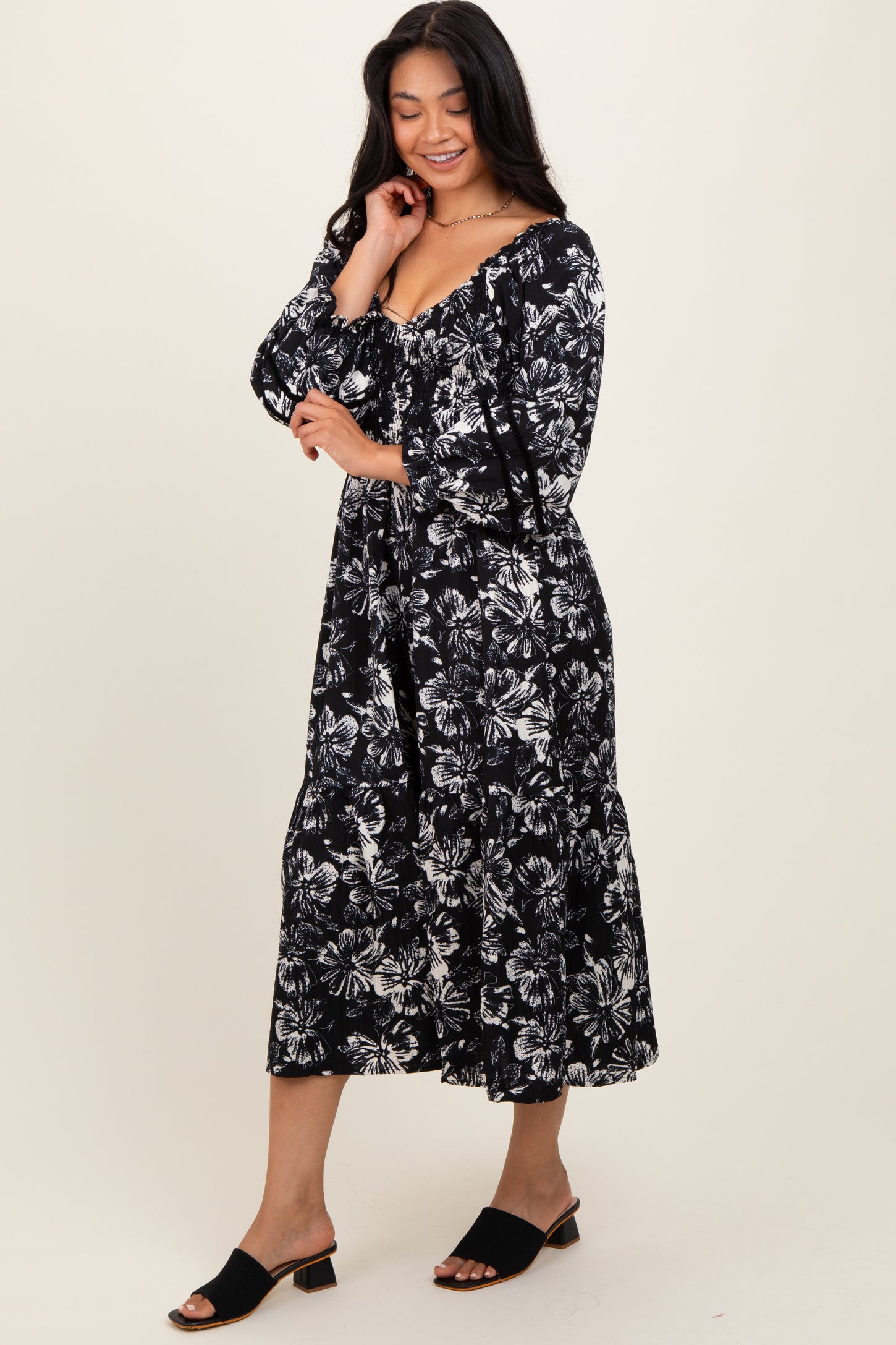woman wearing a black and white floral maxi dress with a v-neckline and long sleeves, standing on a light background