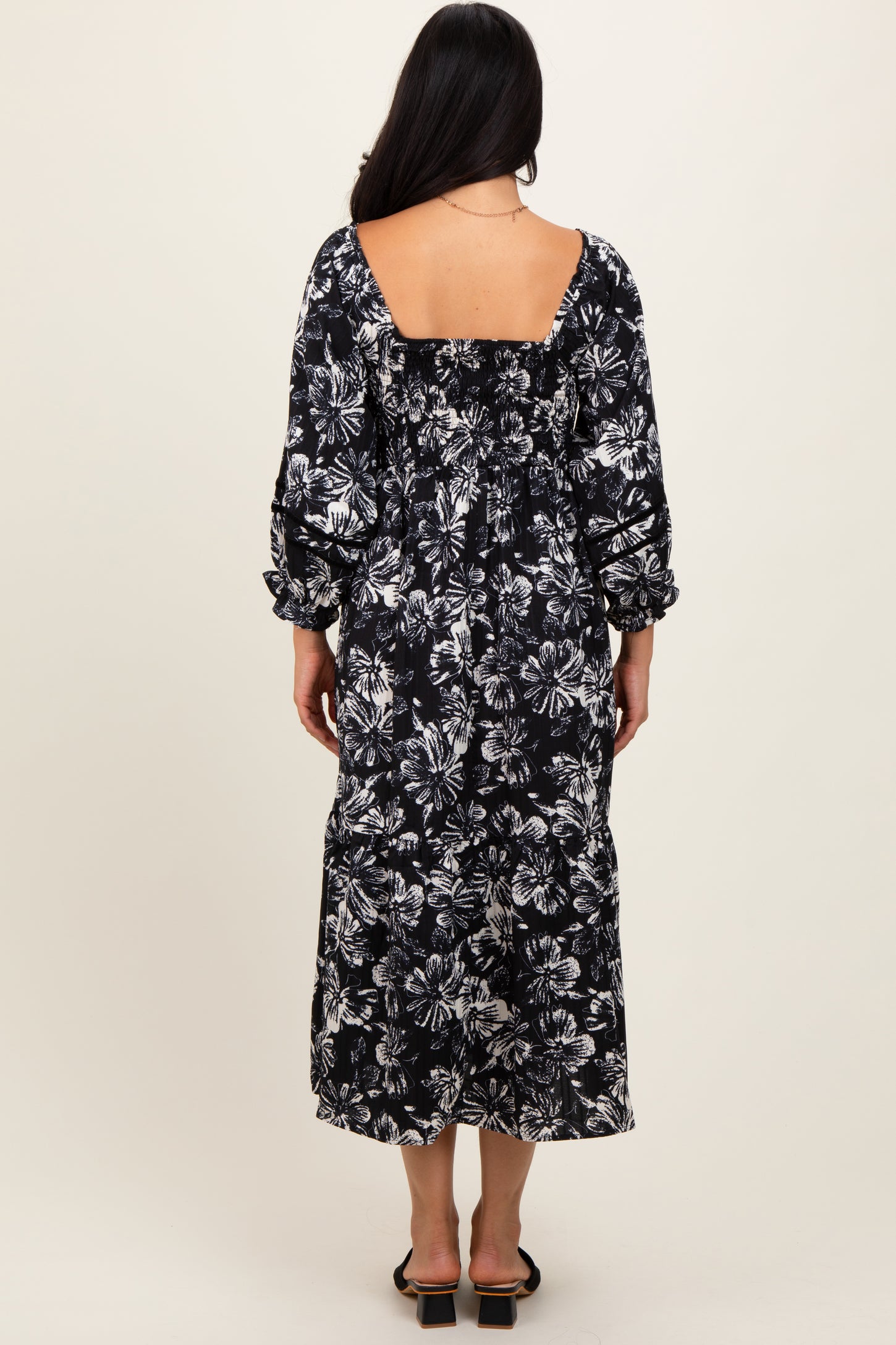 woman wearing a backless black floral maxi dress with long sleeves and a tiered skirt