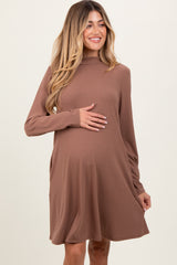 woman wearing a brown long sleeve maternity dress with a high neckline and holding her baby bump