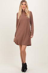 woman wearing a brown long sleeve flared dress with a round neckline and a relaxed fit, paired with black ankle boots
