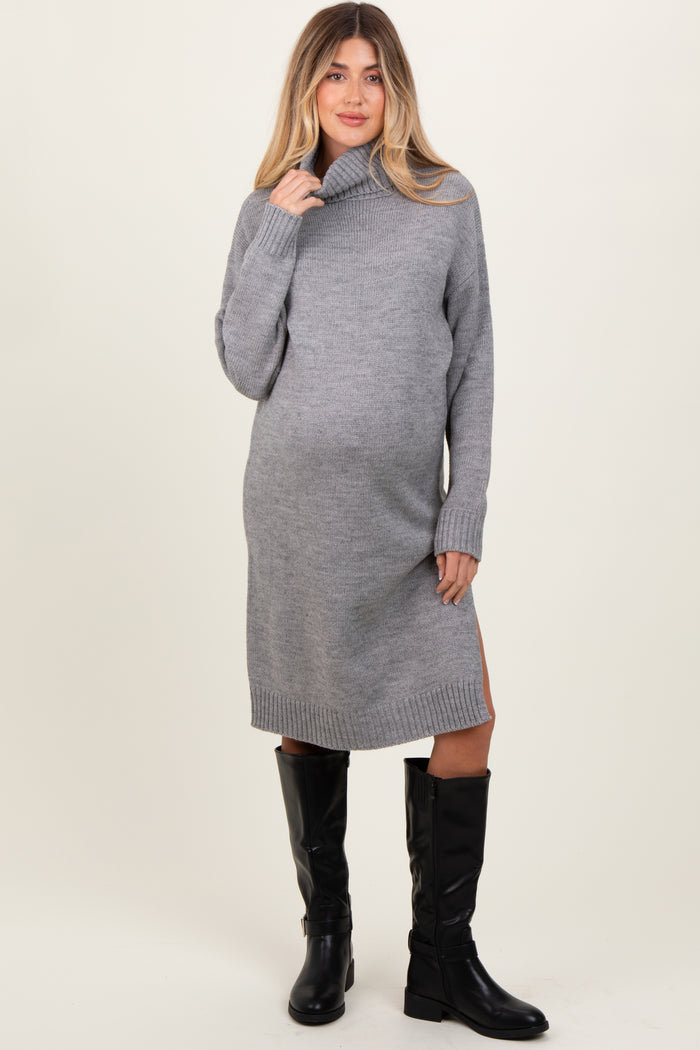 woman wearing a grey turtleneck maternity sweater dress with side slits and knee-high black boots, showcasing her baby bump