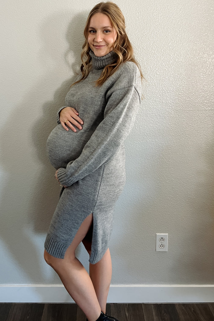 woman wearing a gray maternity sweater dress with turtleneck and side slits, showing her baby bump