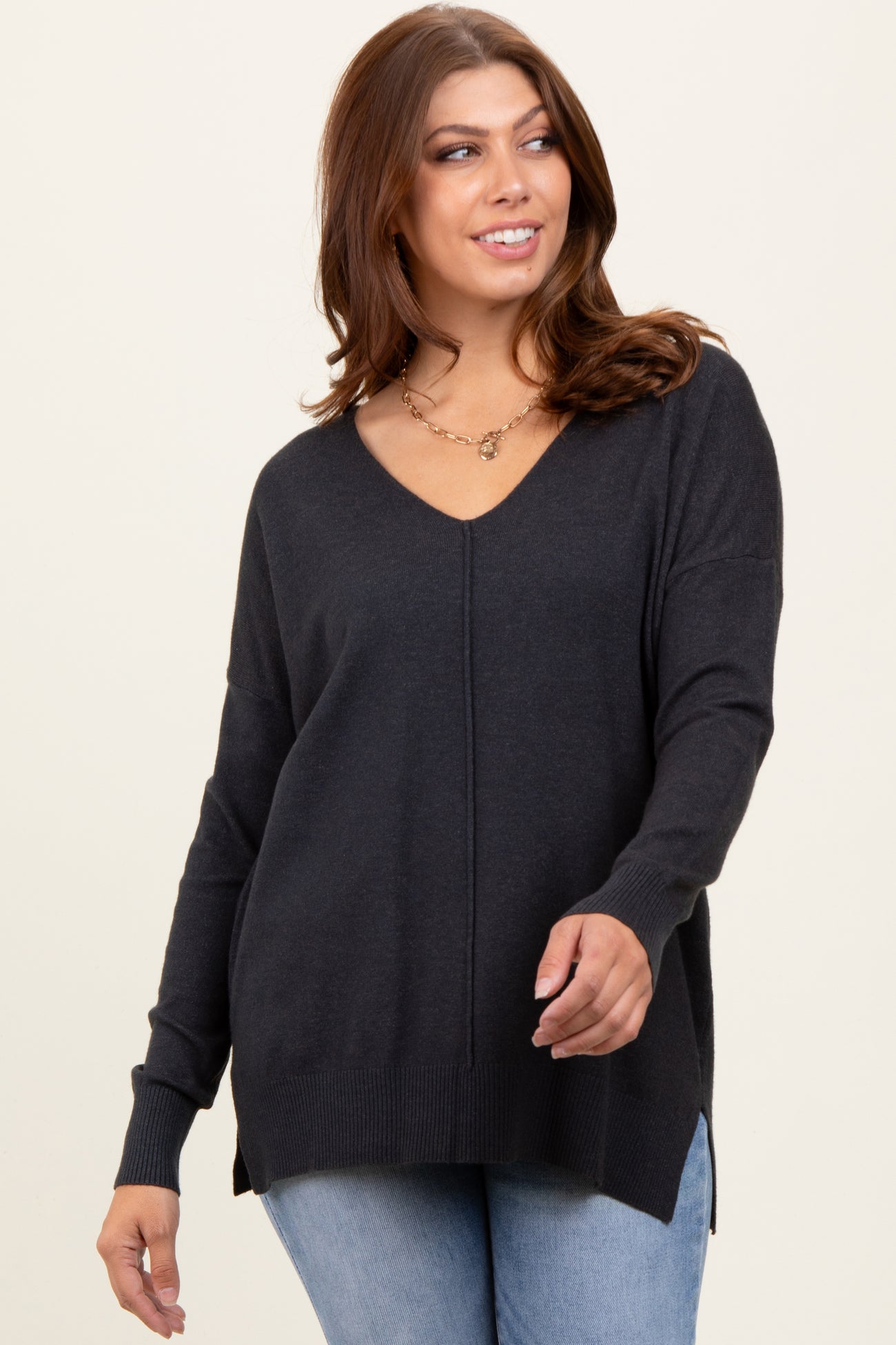 woman wearing a dark gray v-neck oversized sweater with side slits and long sleeves, styled with denim jeans