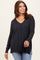 woman wearing a dark gray v-neck oversized sweater with side slits and long sleeves, styled with denim jeans