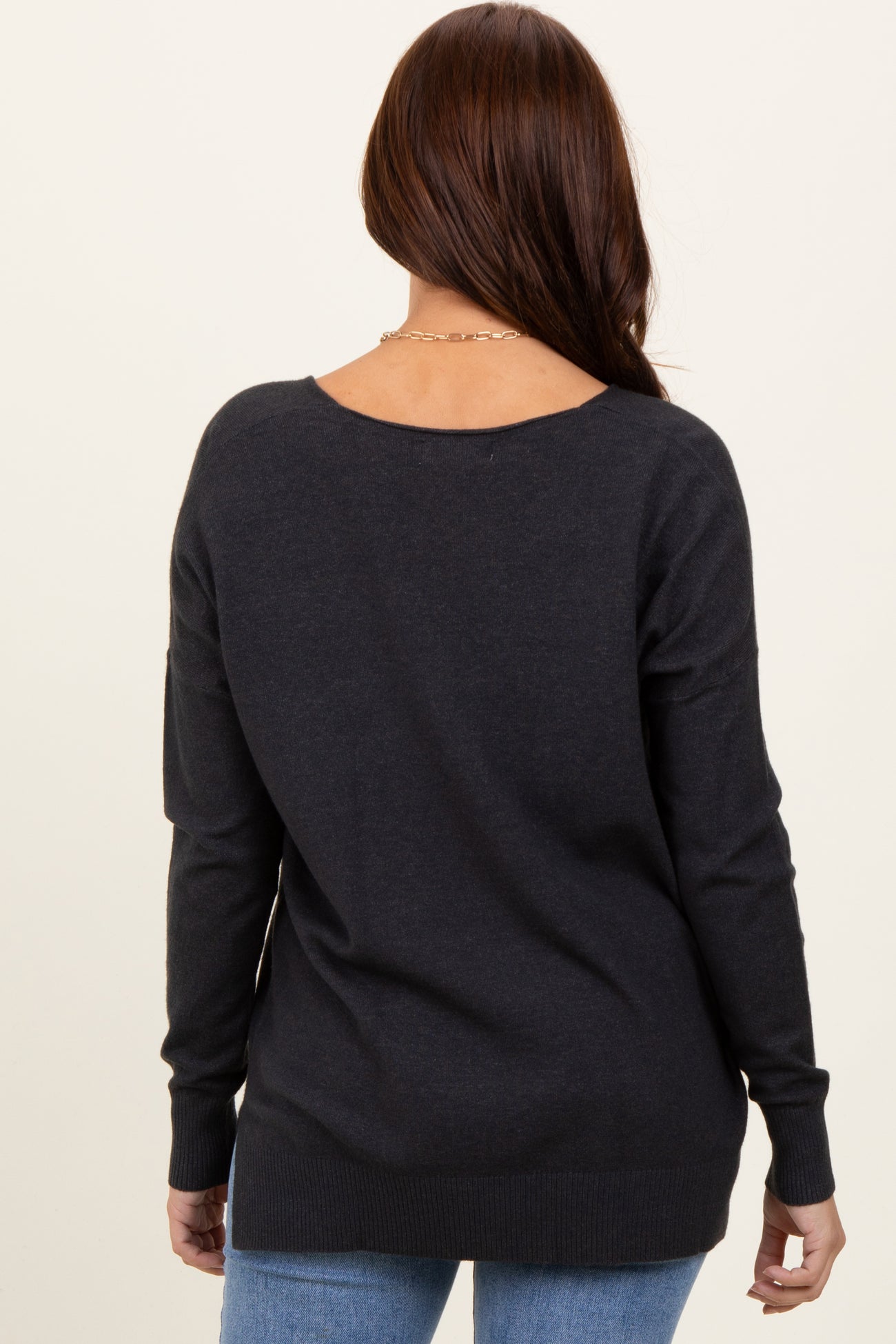 woman wearing a dark gray long sleeve sweater with a relaxed fit and open back, paired with light blue jeans