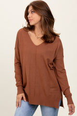woman wearing a brown v-neck oversized sweater with side slits, styled with blue jeans and a chunky necklace