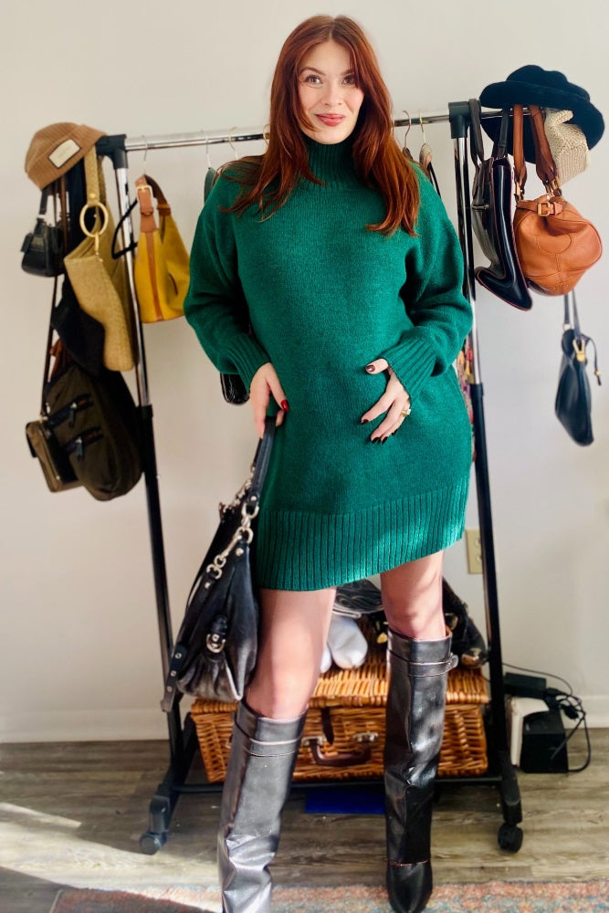 woman wearing a dark green maternity sweater dress with a high neck and ribbed details, showing her baby bump
