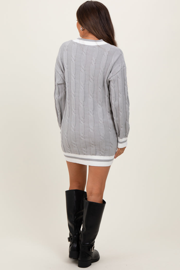 woman wearing a gray cable knit maternity sweater dress with white trim and knee-high black boots, baby bump not visible