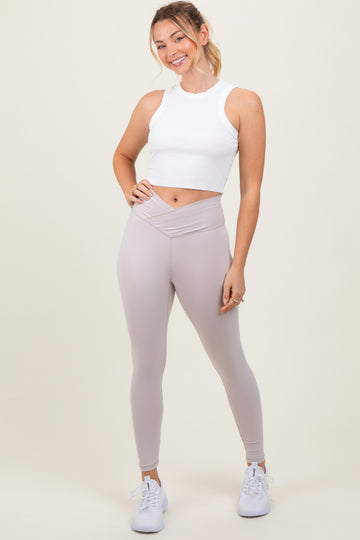 woman wearing a white cropped tank top and light gray high-waisted leggings, posing with a smile