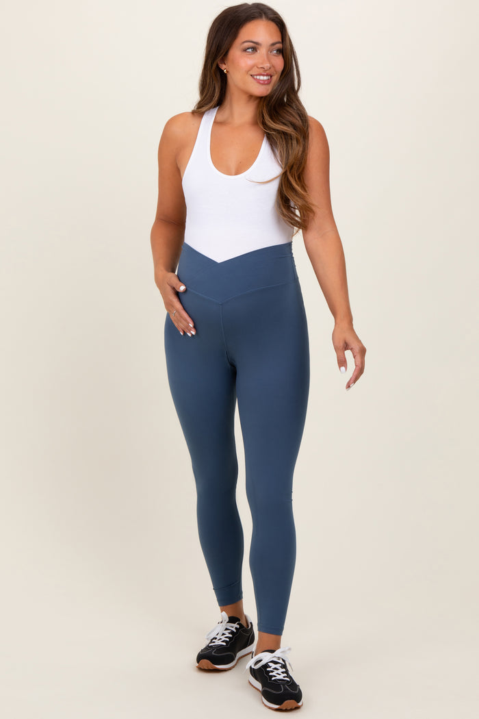 woman wearing a white maternity tank top and blue maternity leggings, showing a baby bump and smiling