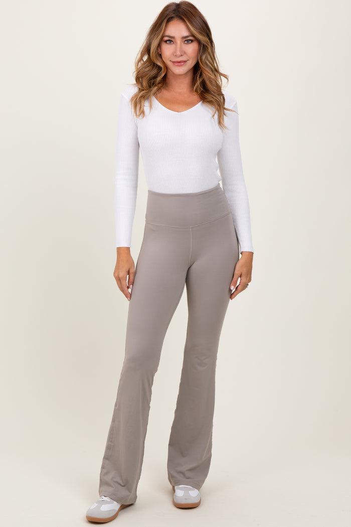 woman wearing a white long sleeve ribbed top and light gray flared pants, standing against a neutral background