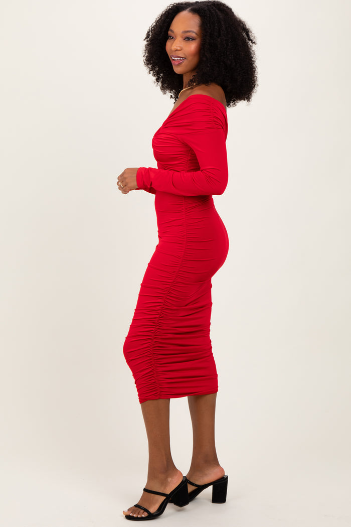 woman wearing a form-fitting red off-the-shoulder midi dress with ruching details and side slit, standing in profile