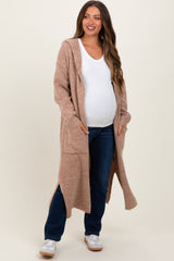 woman wearing a beige long maternity cardigan with pockets and a white top, showcasing her baby bump and styled with jeans