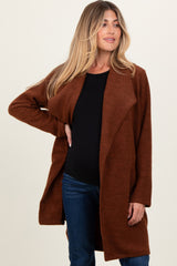 woman wearing a rust-colored maternity wrap coat with a black top and showing her baby bump