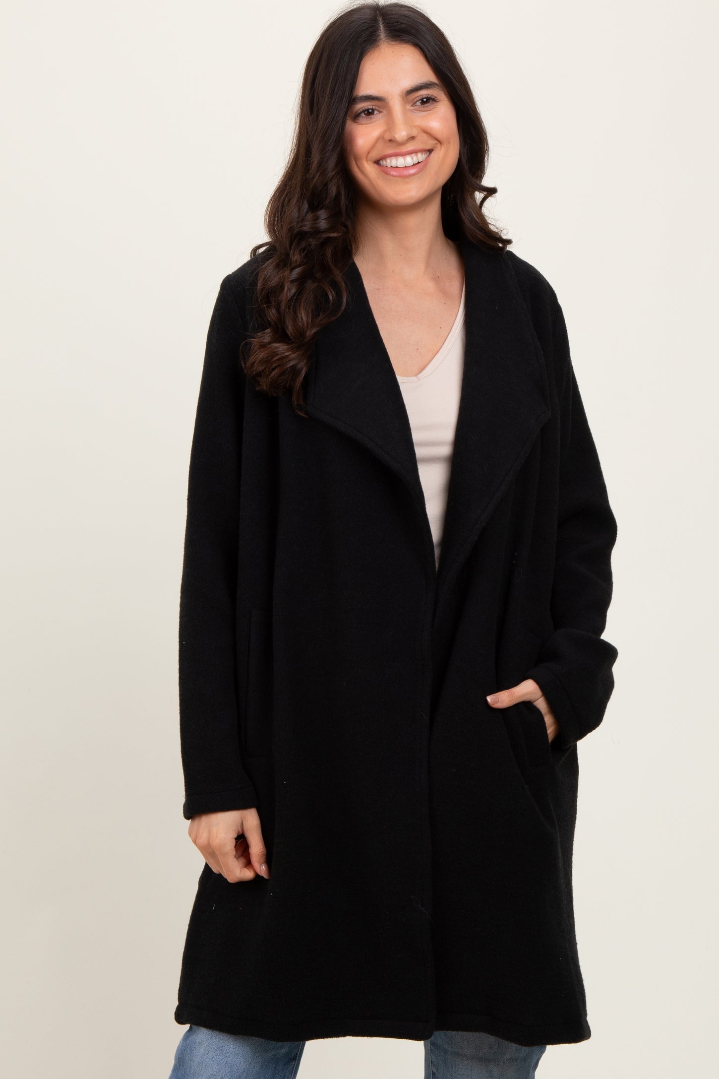 woman wearing a black oversized fleece coat with open front and side pockets, smiling against a neutral background