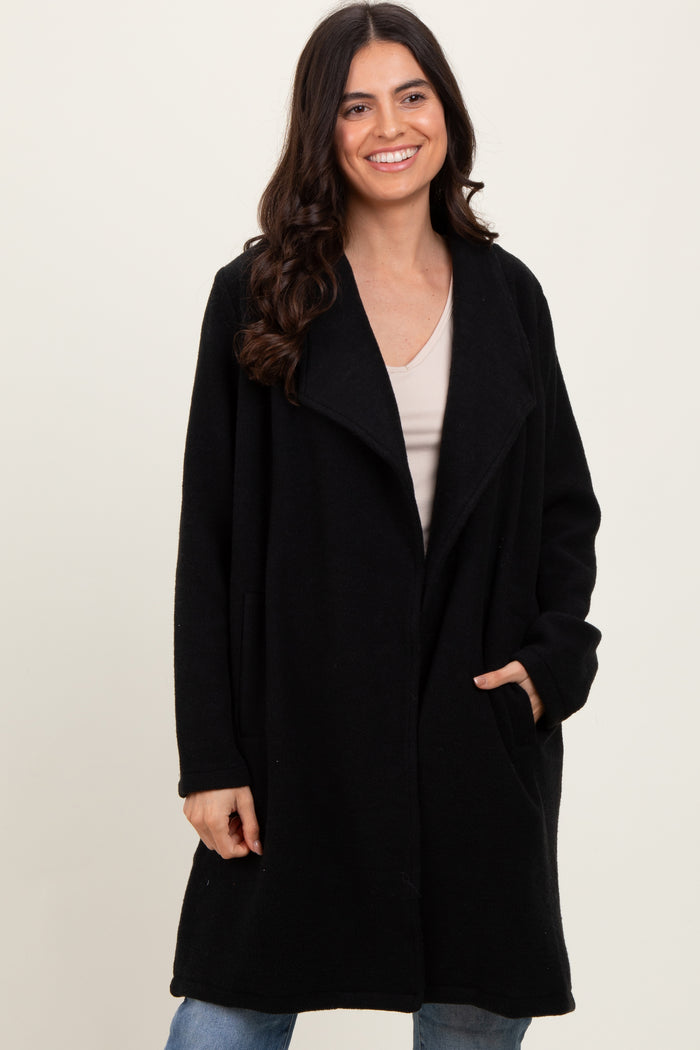 woman wearing a black oversized fleece coat with open front and side pockets, smiling against a neutral background