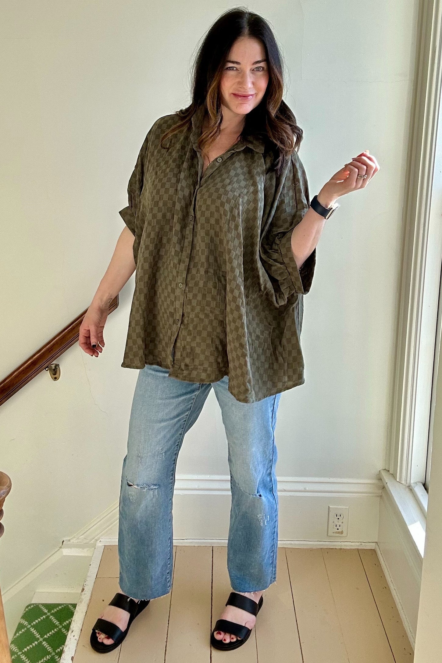 woman wearing a loose-fitting olive green checkered maternity shirt and light blue distressed jeans with black sandals