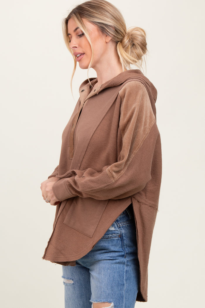 woman wearing a brown oversized hoodie with a front pocket and side slits, styled with distressed denim shorts