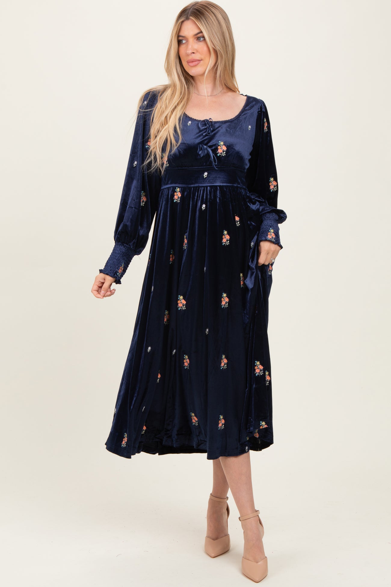 woman wearing a navy blue velvet midi dress with floral embroidery and long sleeves, styled with a tie at the waist