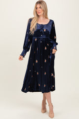 woman wearing a navy blue velvet midi dress with floral embroidery and long sleeves, styled with a tie at the waist