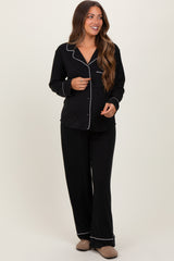 woman wearing a black maternity pajama set with white piping details and long sleeves, standing and smiling