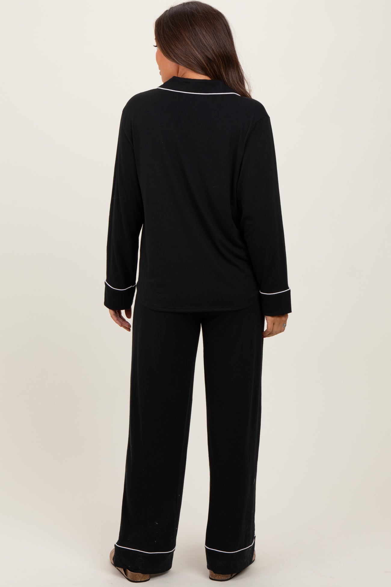 woman wearing a black long sleeve maternity pajama set with white piping details, shown from the back