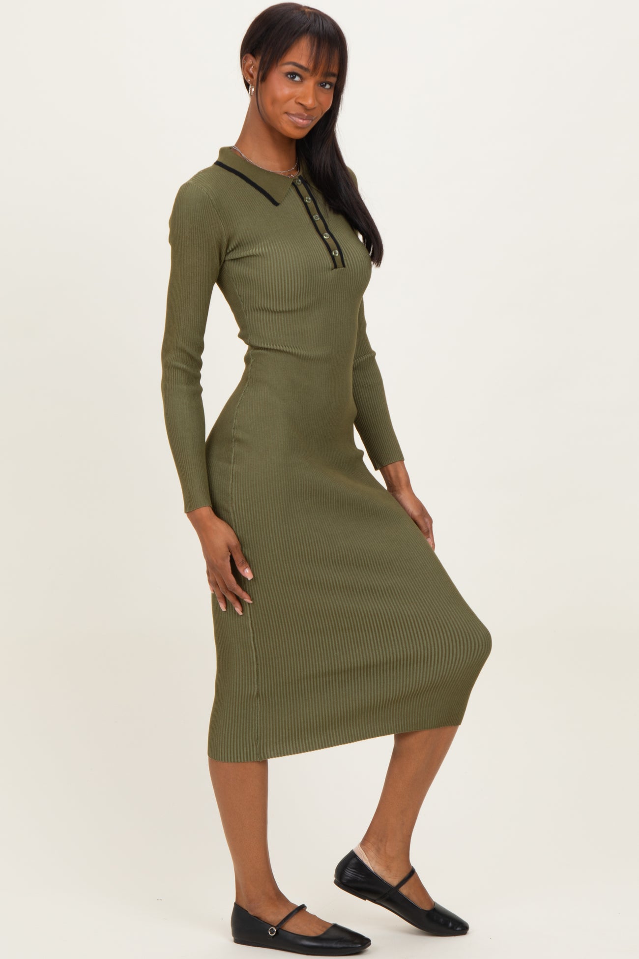 woman wearing a long sleeve olive green ribbed midi dress with a collar and button details, standing with one hand on her hip