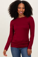 woman wearing a burgundy long sleeve top paired with blue jeans, smiling at the camera