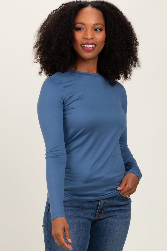 woman wearing a blue long sleeve fitted top and jeans, smiling with curly hair