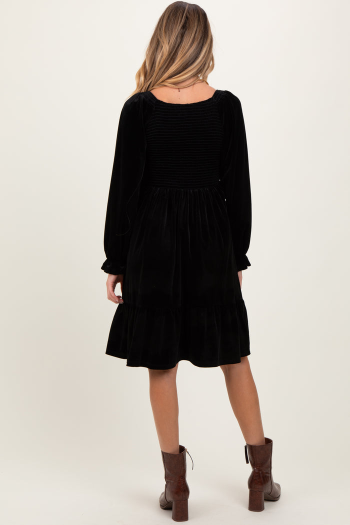 woman wearing a black velvet maternity dress with a smocked back and long sleeves, standing with her back to the camera