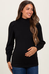 woman wearing a black ribbed maternity top with puff sleeves and holding her baby bump