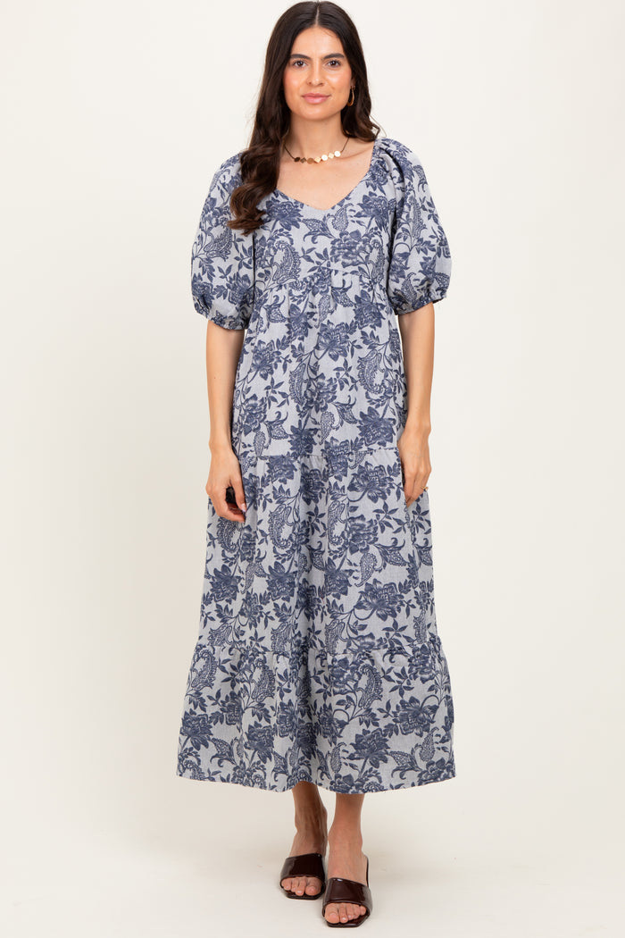 woman wearing a navy blue floral maxi dress with puff sleeves and a v-neckline, standing and smiling