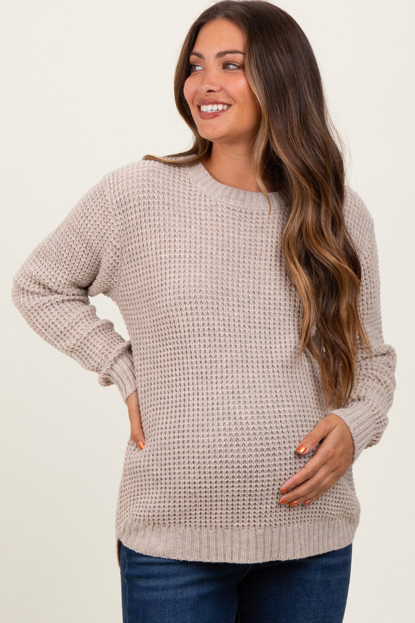 woman wearing a beige knit maternity sweater and holding her baby bump