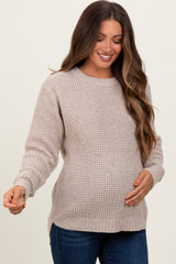 woman wearing a beige knit maternity sweater with a rounded neckline and long sleeves, showing a baby bump