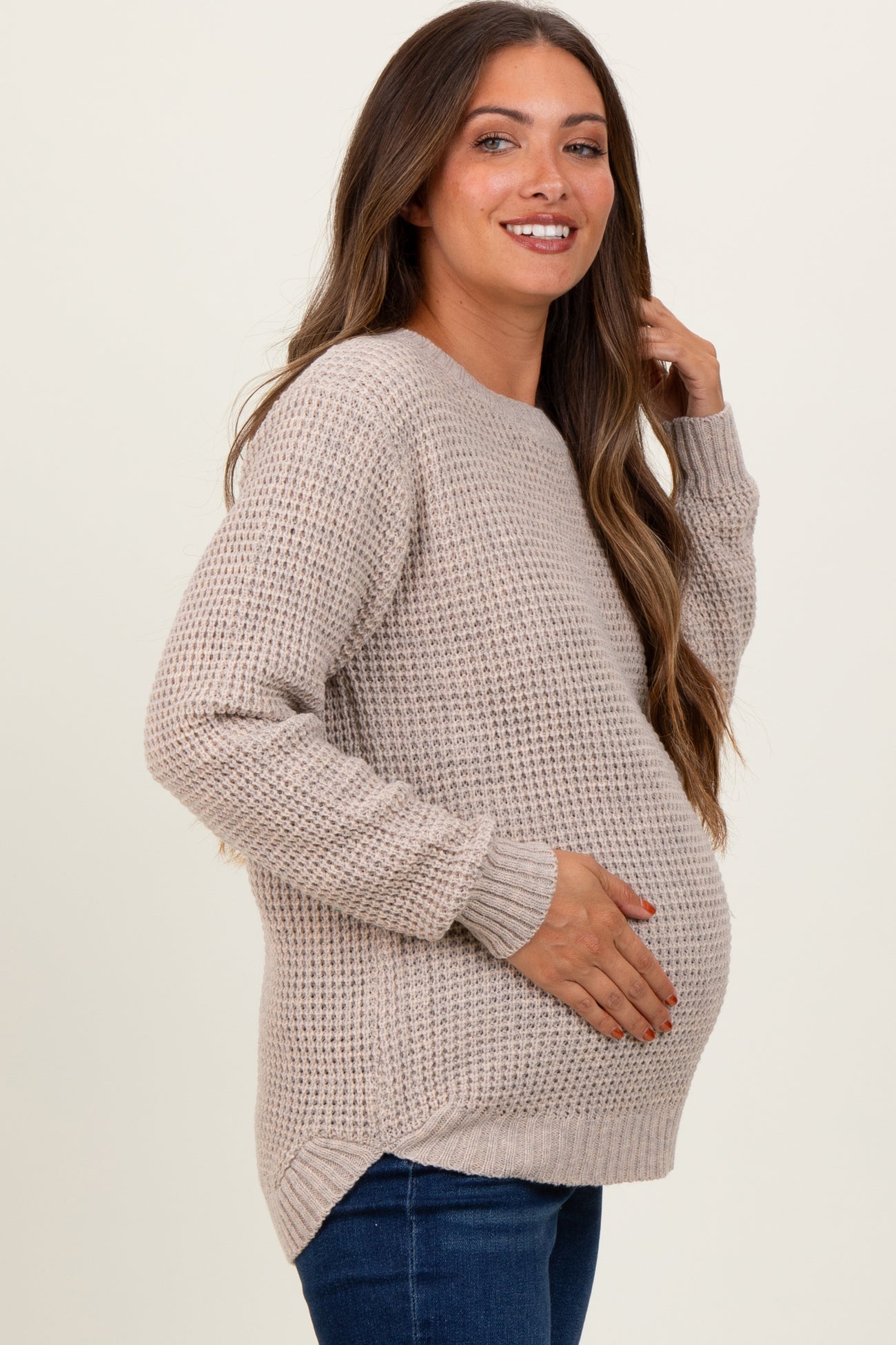 woman wearing a light beige knitted maternity sweater and holding her baby bump