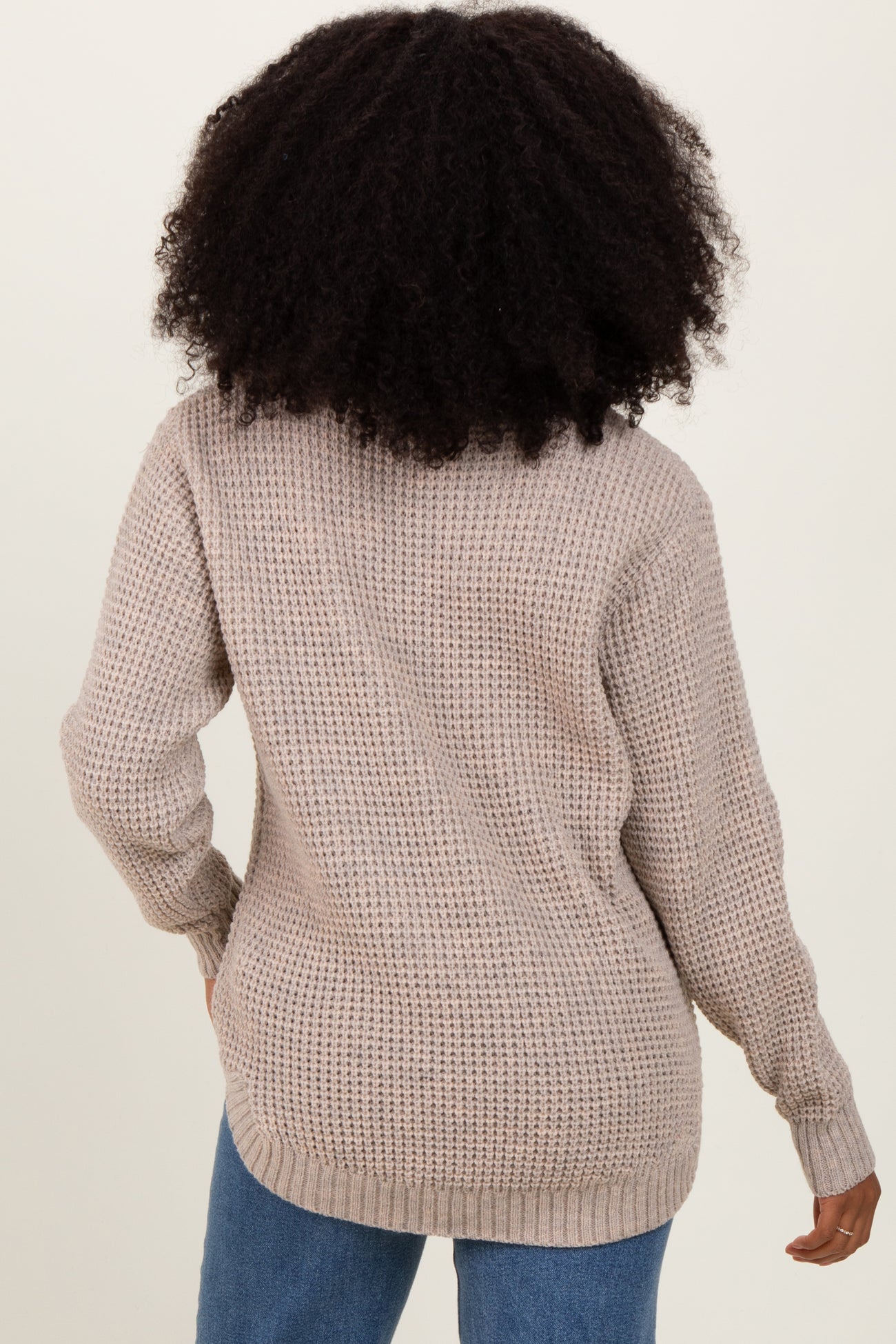 woman wearing a beige oversized knit sweater from the back, paired with light blue jeans