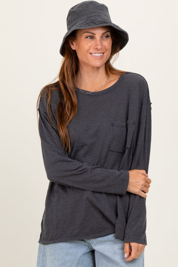woman wearing a dark gray long sleeve top with a pocket and blue jeans, smiling and wearing a gray bucket hat