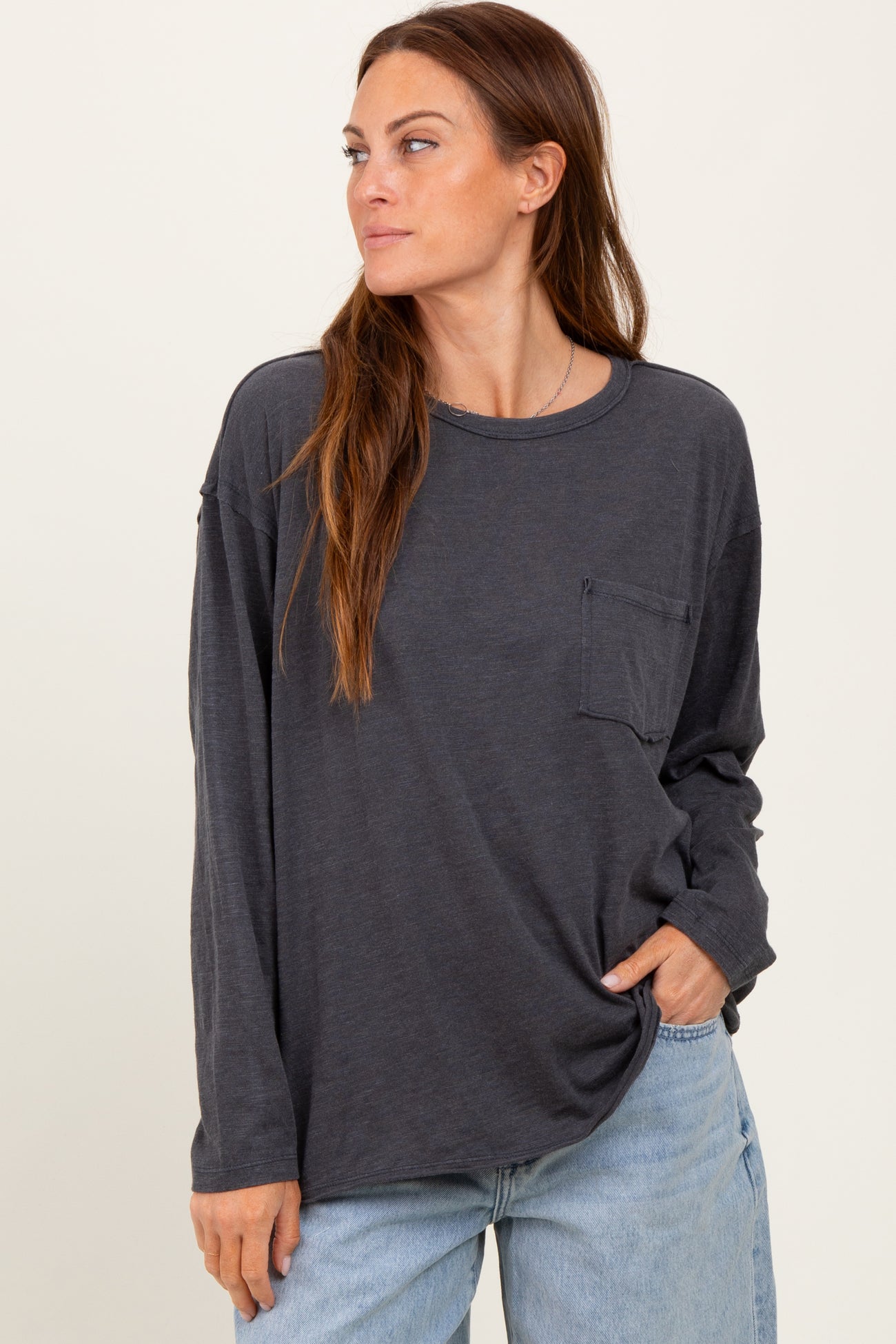 woman wearing a dark gray long sleeve t-shirt with a pocket and relaxed fit, styled with light blue jeans