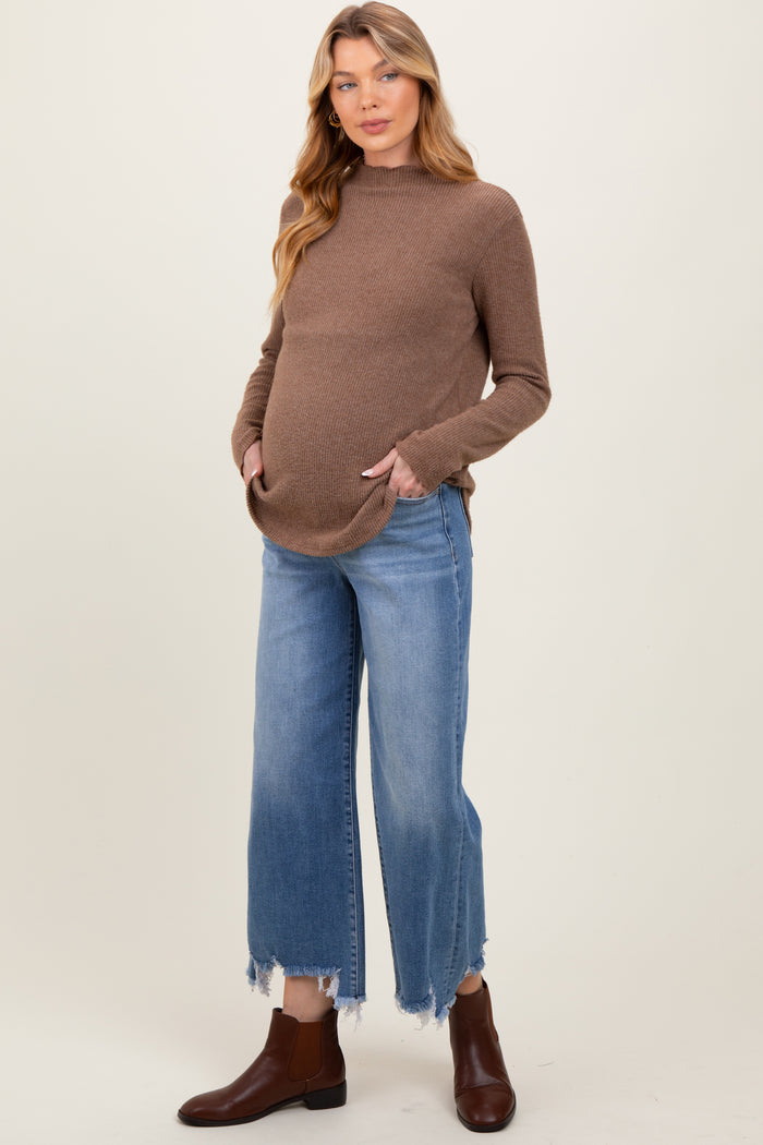 woman wearing a brown maternity sweater with pockets and blue frayed hem denim jeans, showing her baby bump