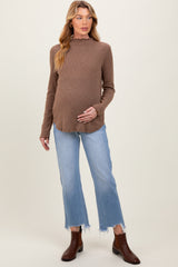 woman wearing a brown maternity sweater and blue distressed jeans, showcasing her baby bump
