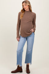 woman wearing a brown ribbed maternity sweater and light blue cropped jeans, holding her baby bump