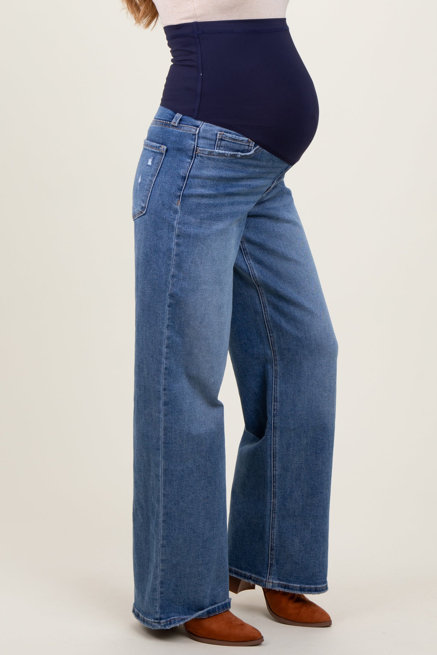 woman wearing a pair of blue wide-leg maternity jeans with a supportive waistband, showcasing her baby bump.