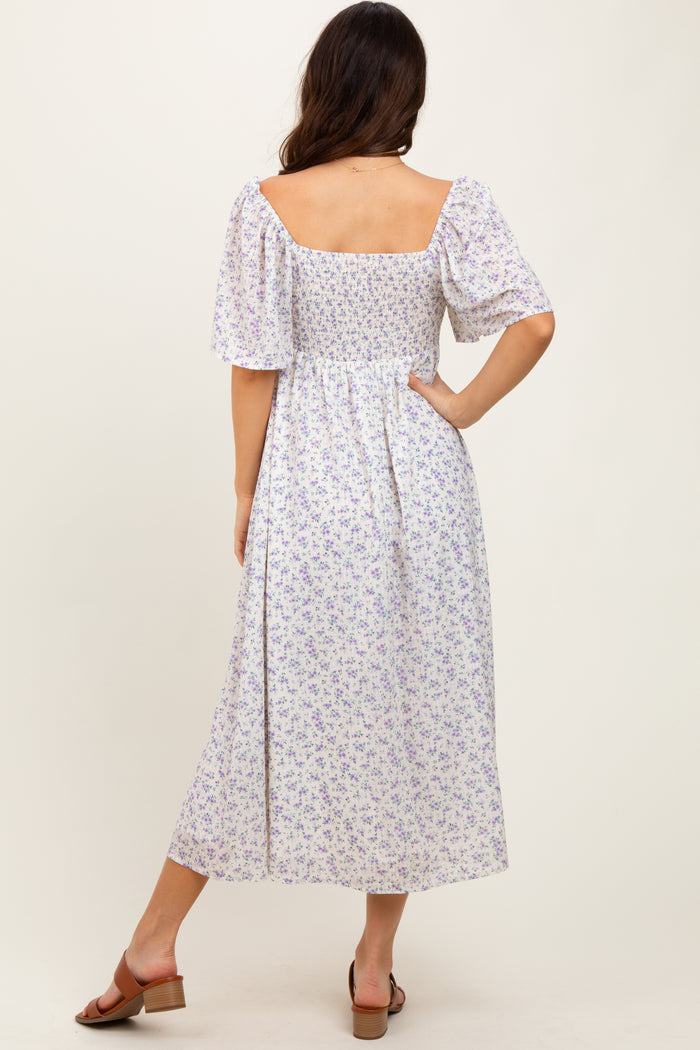 woman wearing a white floral midi dress with short sleeves and a smocked back, standing with her back to the camera