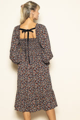 woman wearing a black floral midi dress with a back tie detail and puff sleeves
