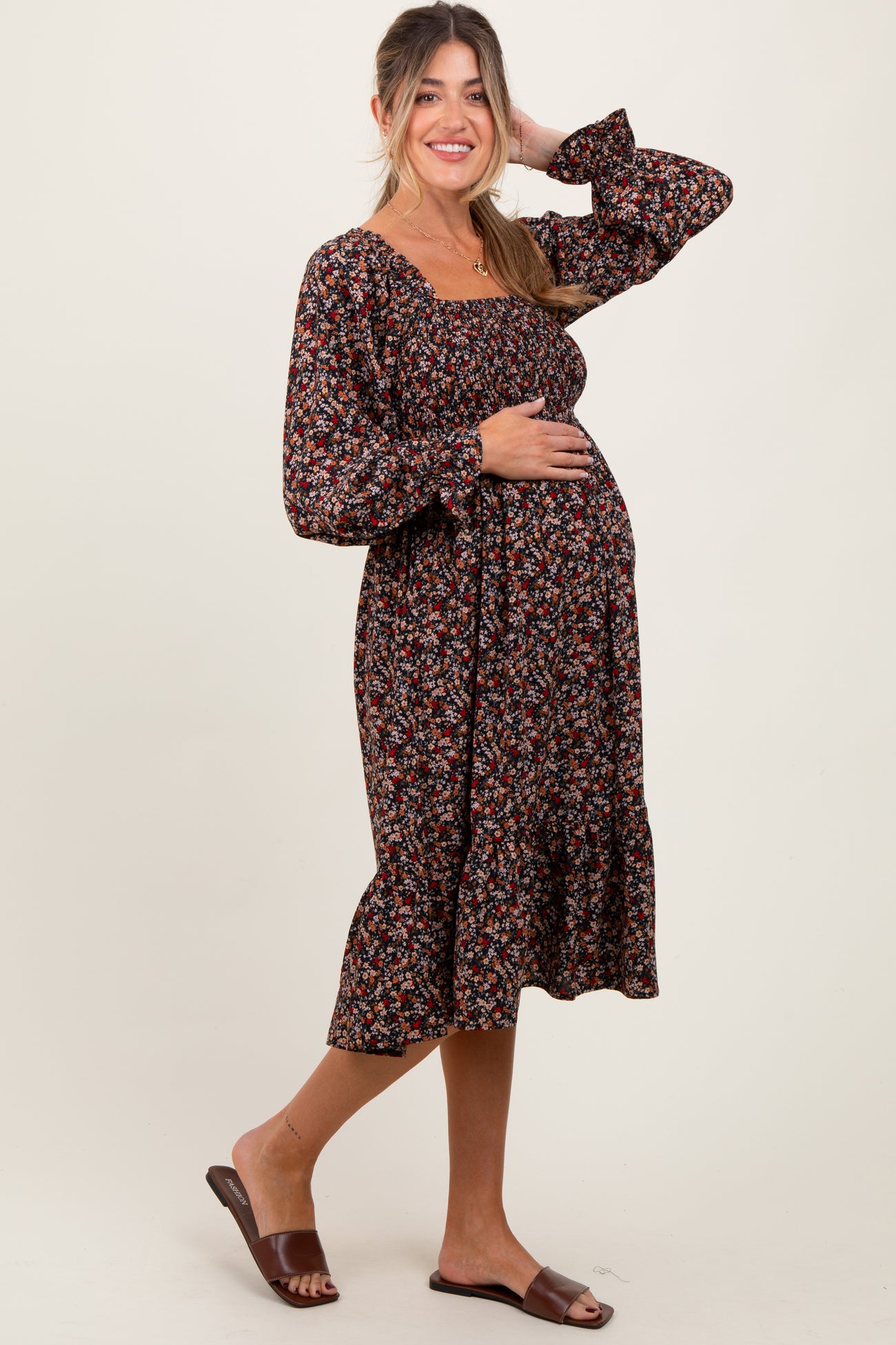 woman wearing a black floral maternity dress with long sleeves and a ruffled hem, gently cradling her baby bump