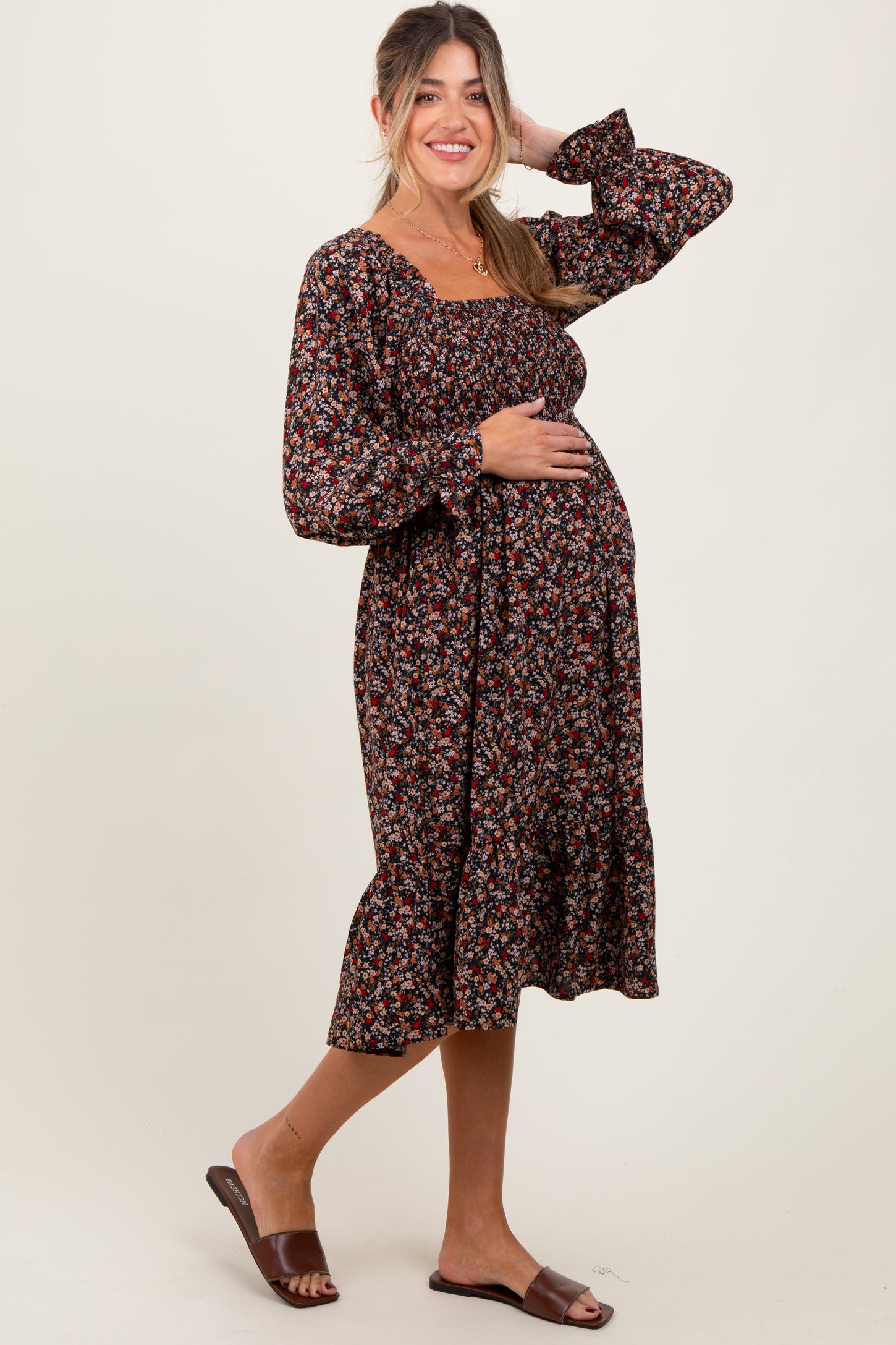 woman wearing a black floral maternity dress with long sleeves and a ruffled hem, gently cradling her baby bump