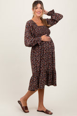 woman wearing a black floral maternity dress with long sleeves and a ruffled hem, gently cradling her baby bump
